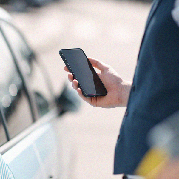 Närbild på en hand som håller en mobil vid sidan av en bil