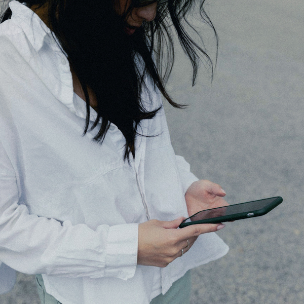 Kvinna med vit skjorta och mörkt hår tittar ner i sin mobilskärm