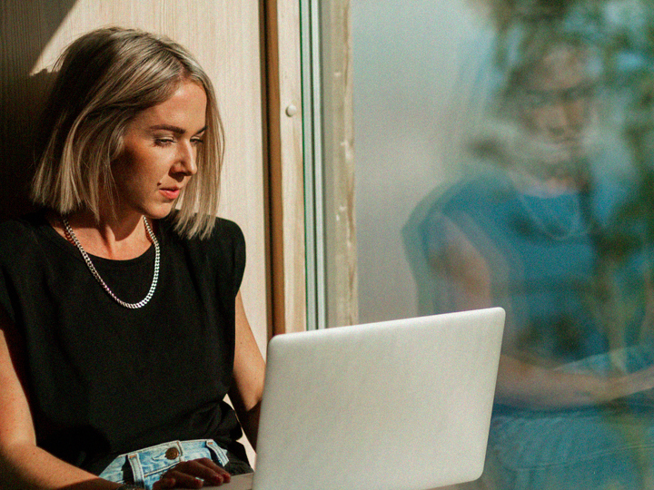 Ung kvinna sitter med laptop i fönster
