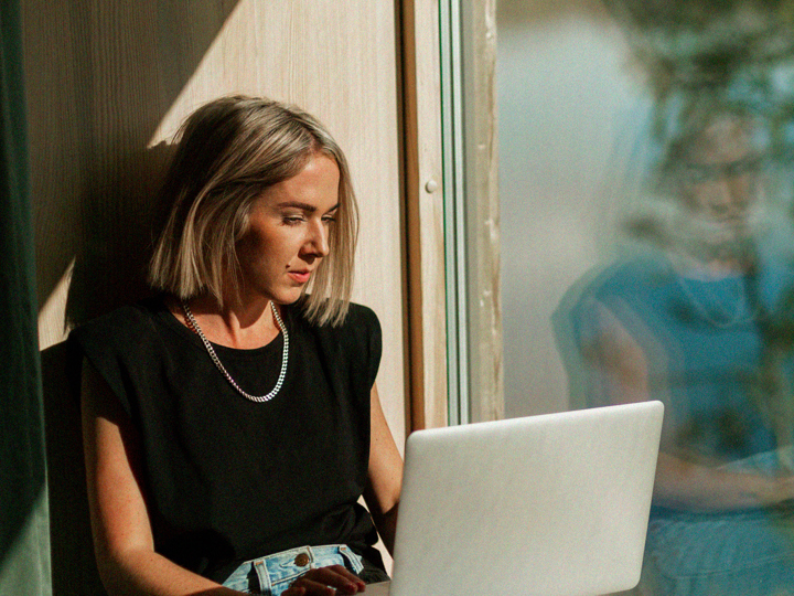 Ung kvinna sitter med sin laptop i ett soligt fönster 