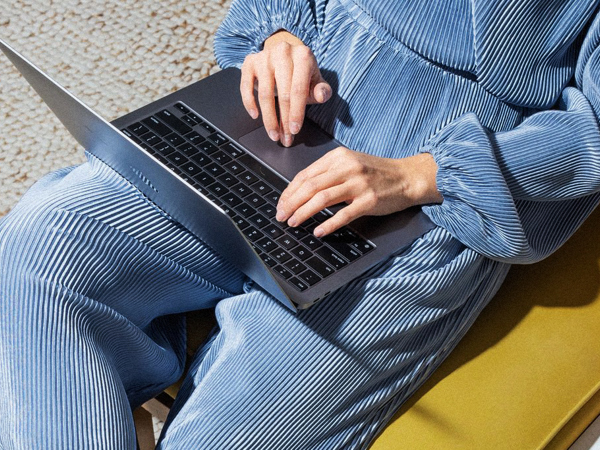 Närbild på en laptop i knäet på en person i blåa kläder